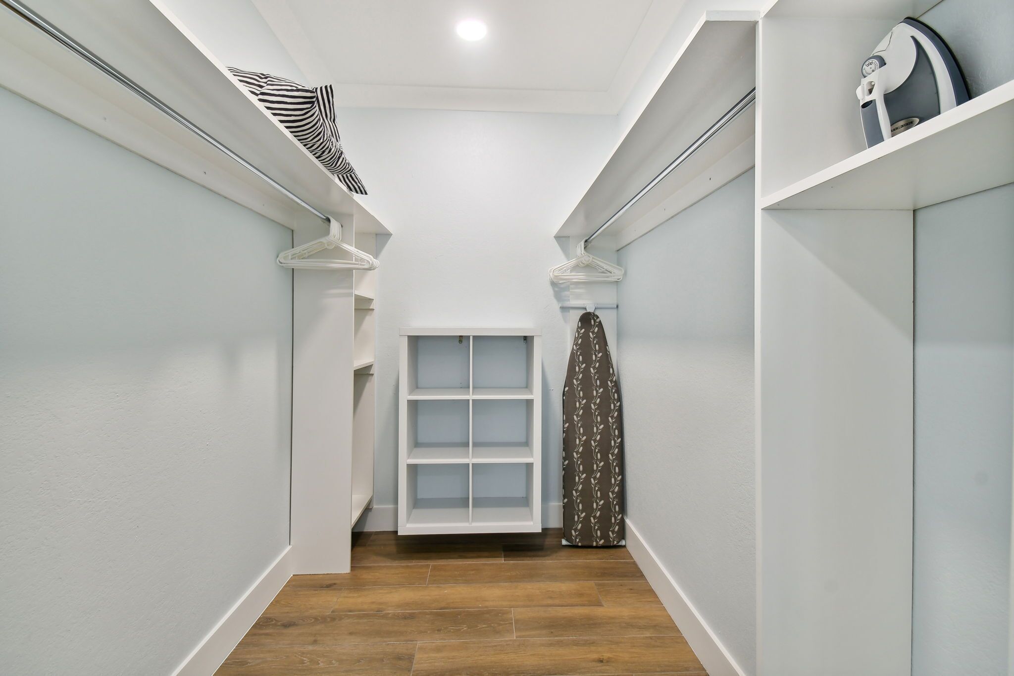 Un couloir étroit aux murs blancs et au plancher en bois. Des étagères blanches se trouvent sur le côté droit, et une porte blanche se trouve au fond.