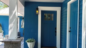 Ein blaues Haus mit weißer Tür, einer Stein Säule und einem Blumentopf.