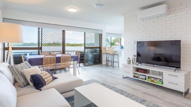 A modern living room with a large TV, white furniture, and a balcony with a view. - Relax & unwind in the "Beach House" (Maroochydore)