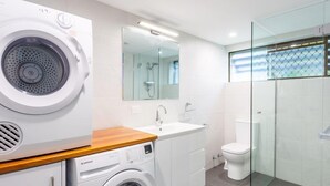 A modern bathroom with a washing machine, a sink, a toilet, and a glass-enclosed shower. - Relax & unwind in the "Beach House" (Maroochydore)
