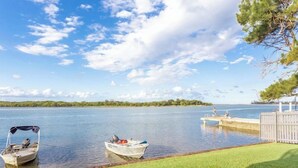 A calm lake with two boats docked at a wooden pier, surrounded by a grassy area and a wooden fence. - Relax & unwind in the "Beach House" (Maroochydore)