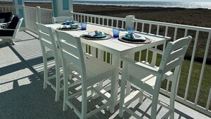A covered outdoor dining area with white furniture and a view of the beach. - "Above the Waves" - BEACH FRONT (Galveston)