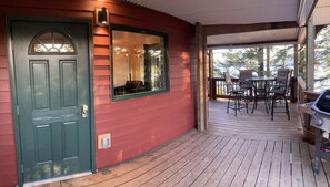 A wooden deck with outdoor furniture, a green door, and a window with a view of trees.