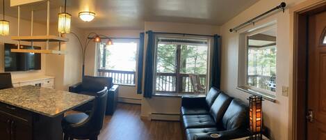 A modern kitchen with a granite countertop, black leather seating, and a large window with a view of trees.