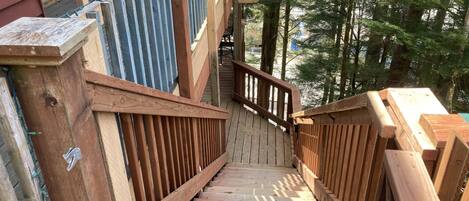 A wooden staircase with railings leading up to a building, surrounded by trees.