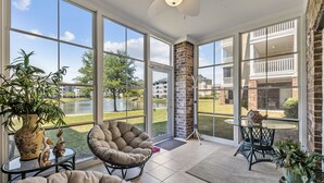A sunroom with large windows, a brick fireplace, and a view of a golf course. - Cozy Condo//Pool/Workspace/Dogs Stay for Free! (Myrtle Beach)