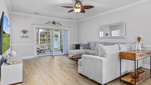 A modern living room with a grey sofa, a wooden coffee table, a ceiling fan, and a large mirror. - Cozy Condo//Pool/Workspace/Dogs Stay for Free! (Myrtle Beach)