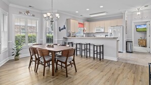 A modern kitchen with white cabinets, a central island, and a dining area with wooden chairs and a table. - Cozy Condo//Pool/Workspace/Dogs Stay for Free! (Myrtle Beach)