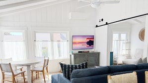 A modern living room with a large blue sofa, a dining table with chairs, and a television on a cabinet.