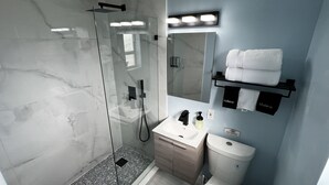 Un baño moderno con cabina de ducha de vidrio, un tocador con lavabo y espejo, y un inodoro.