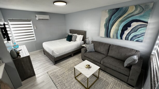 Un dormitorio moderno con una cama, un sofá gris, una mesa de centro blanca y un cuadro abstracto grande en la pared.