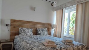 Ett sovrum med en sänggavel i trä, en säng med blommigt sänglinne, två sänglampor, ett nattduksbord och ett fönster med gardiner.