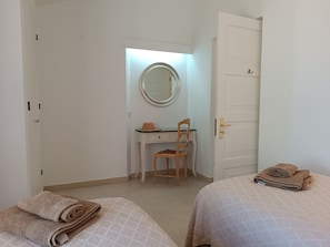 A bedroom with two beds, a desk with a chair, a mirror, and a door.