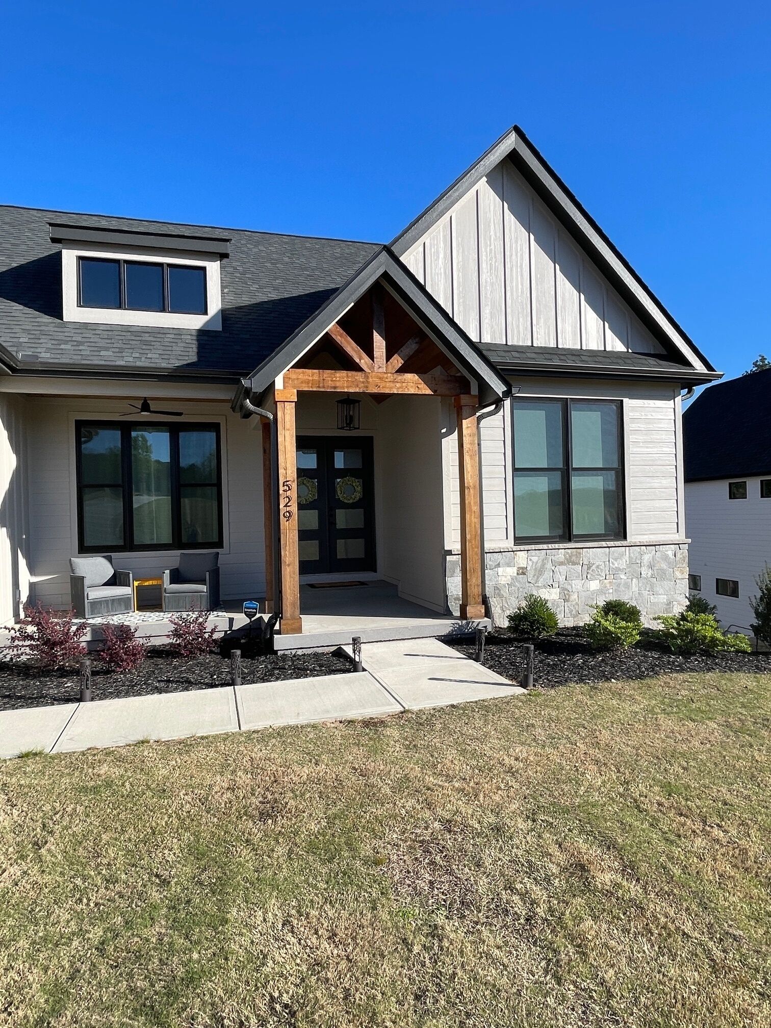 A modern two-story house with a covered porch, large windows, and a stone foundation.