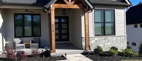 A modern two-story house with a covered porch, large windows, and a stone foundation.