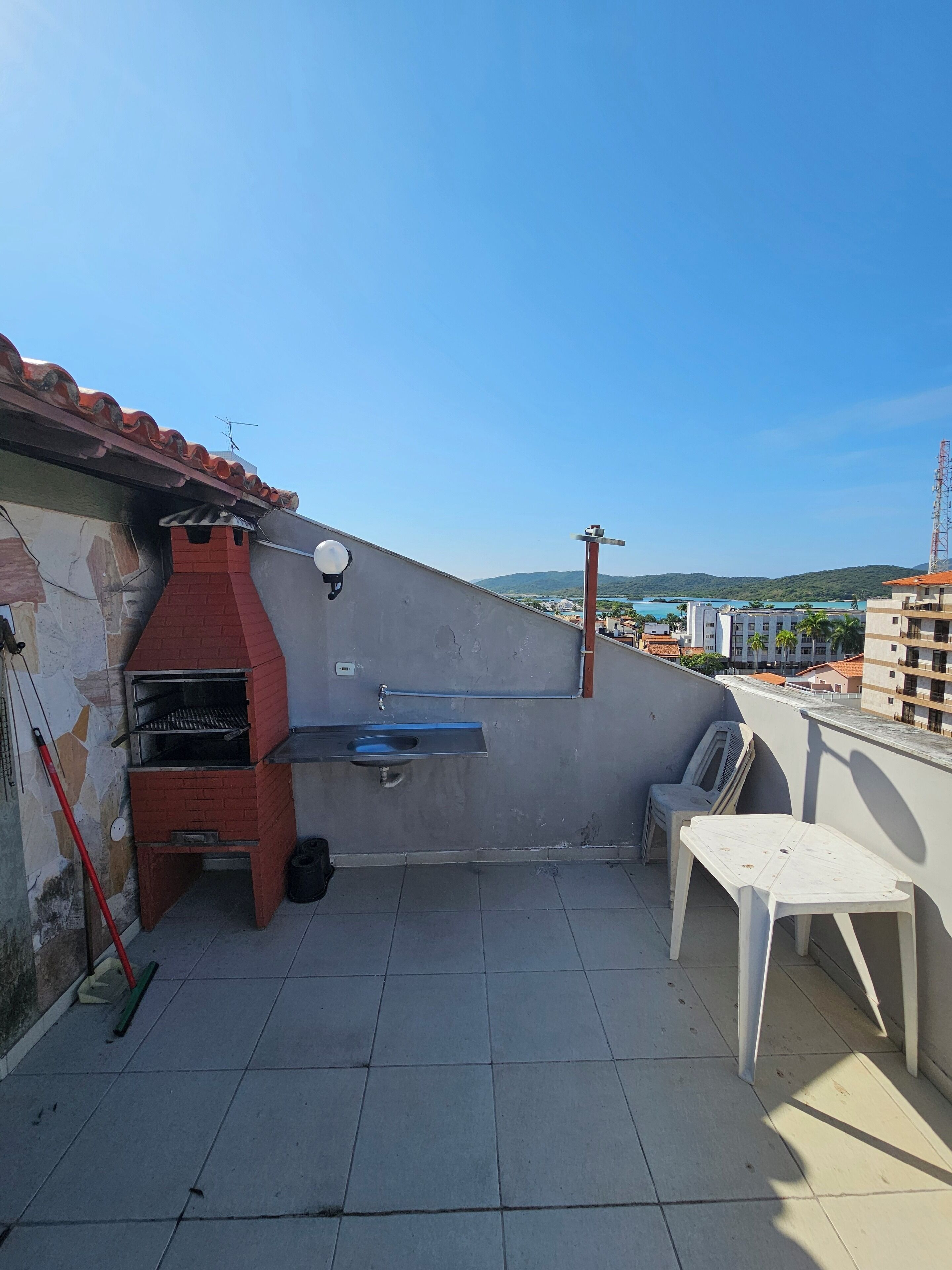 Une terrasse sur le toit avec un barbecue en briques, un évier et une table blanche.