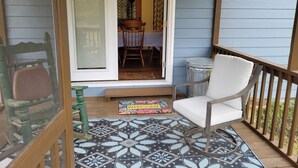 Un porche avec une chaise blanche, un paillasson et un tapis à motifs.