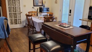Un coin repas comprenant une table en bois, deux chaises, un ventilateur de plafond et un four à micro-ondes posé sur un petit meuble.