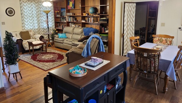 Un salon chaleureux avec un canapé, une table à manger et une bibliothèque remplie de livres et d’objets décoratifs.
