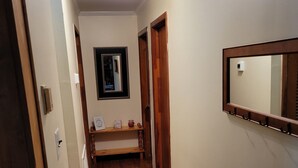 Un couloir étroit avec un plancher en bois, un banc, un miroir et une porte.