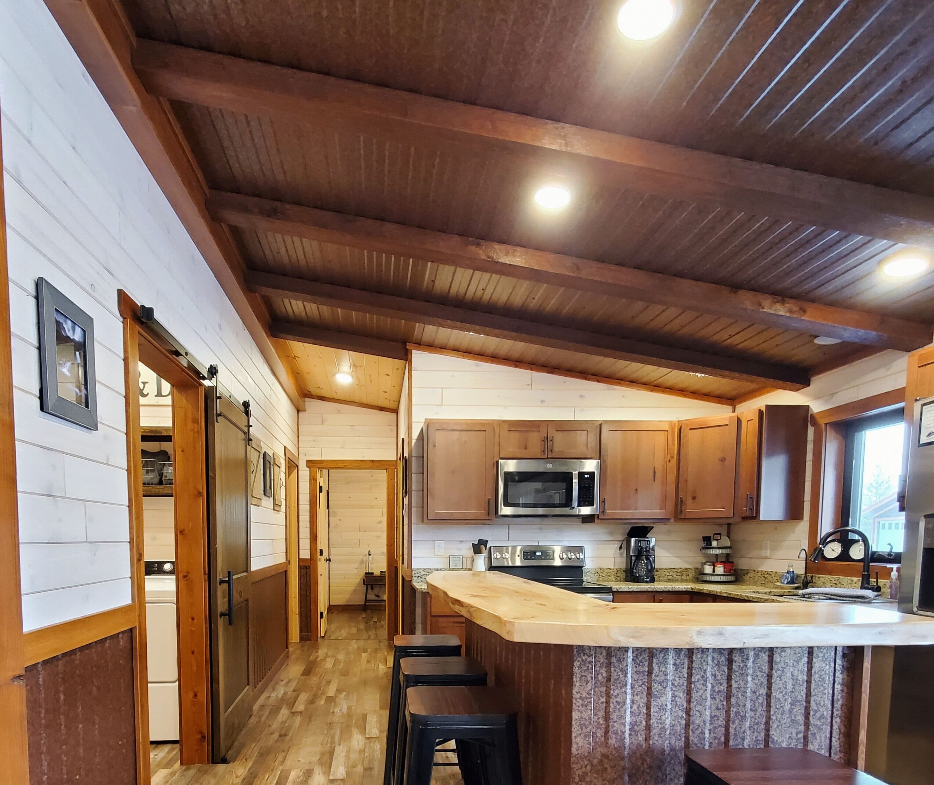 A kitchen with wooden cabinets, a microwave, and a bar area with stools.