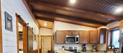 A kitchen with wooden cabinets, a microwave, and a bar area with stools.