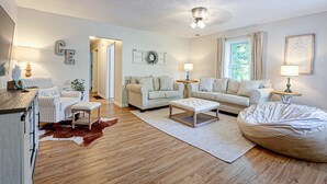 A spacious living room with a wooden floor, a large white sofa, a smaller sofa, a coffee table, and a bean bag.