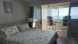 Een hotelkamer met een bed, een stoel, een tafel en uitzicht op zee.