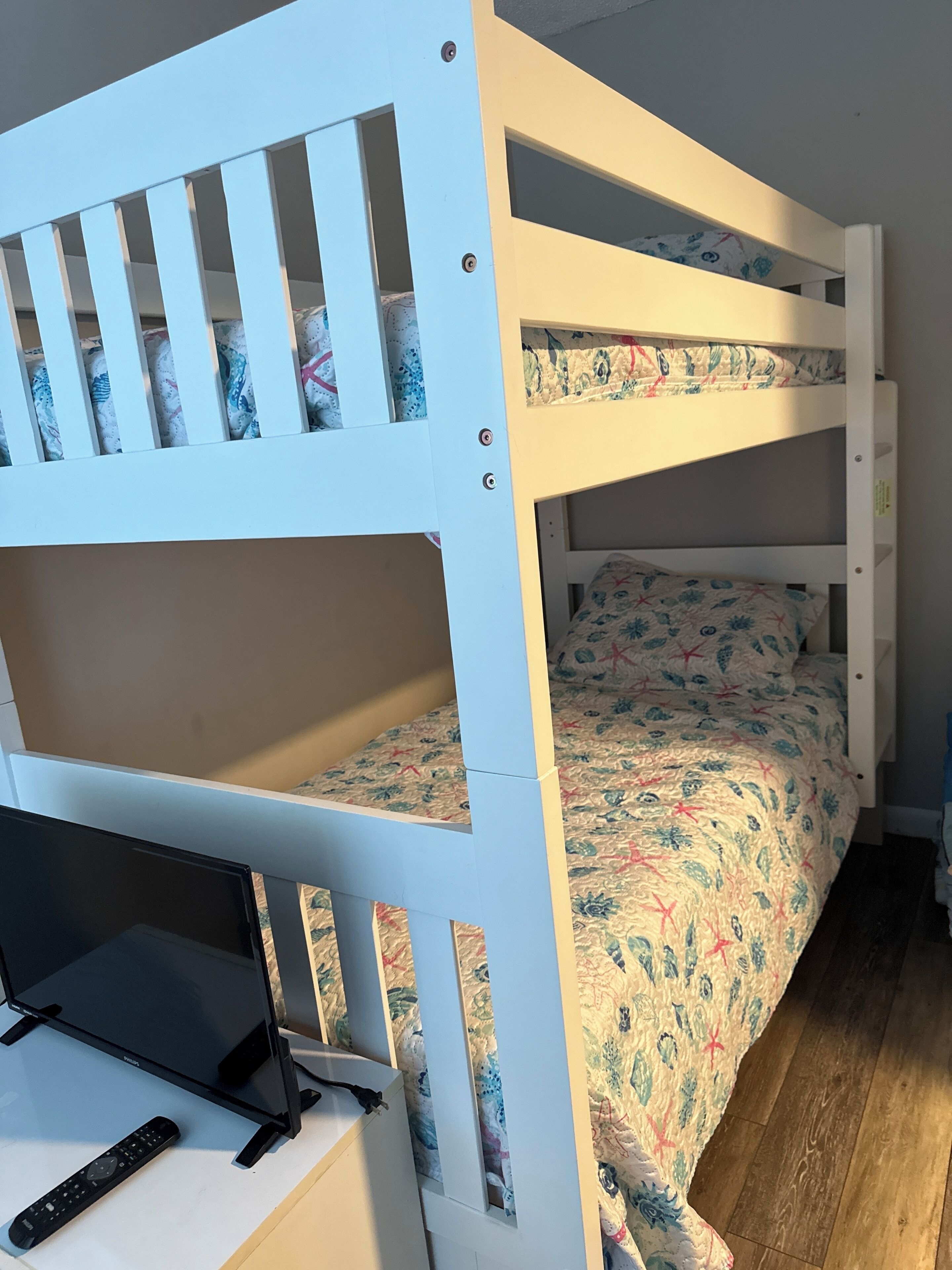 Un lit superposé avec un lit inférieur et un bureau équipé d’un ordinateur portable et d’une télécommande.
