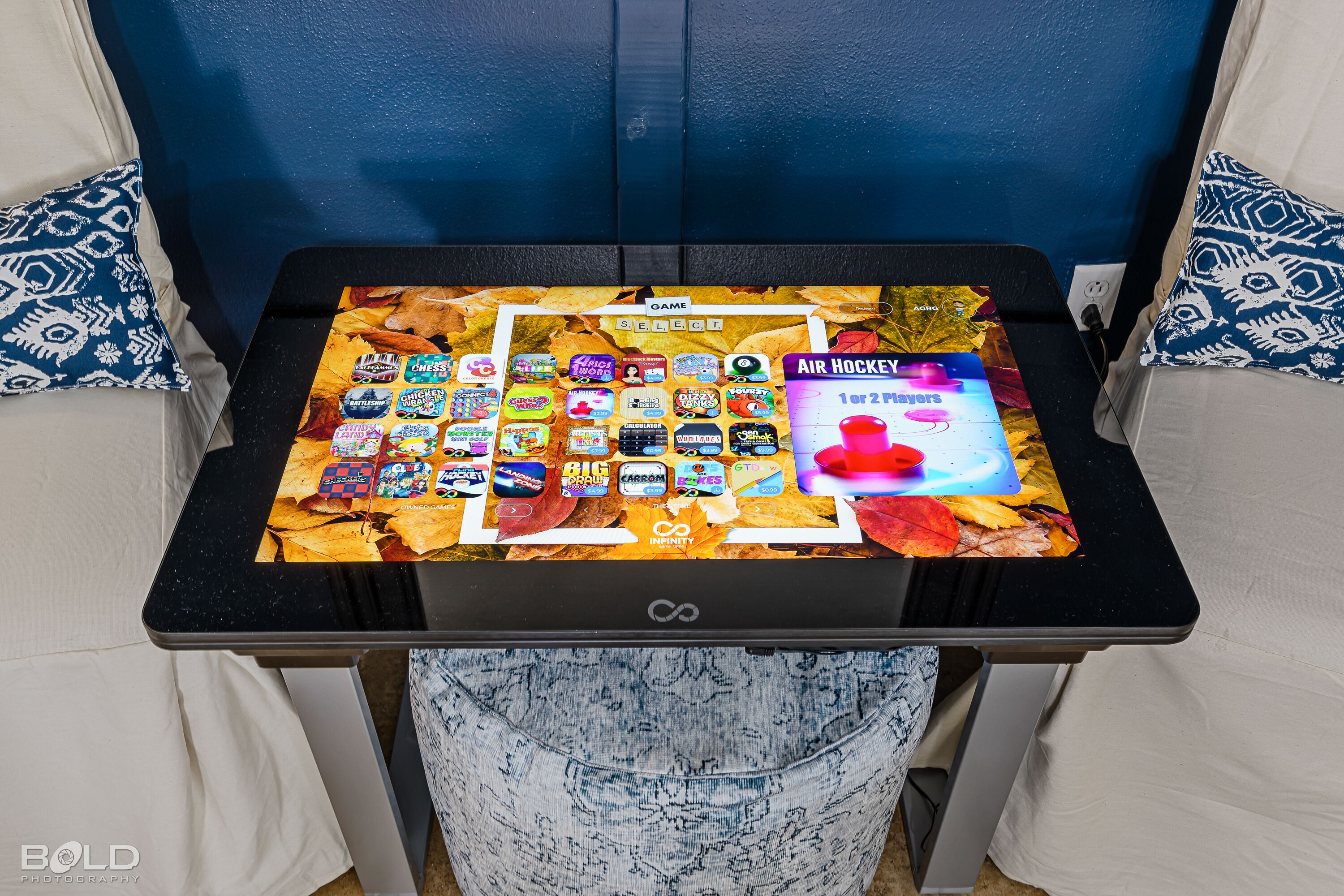 A table with a game selection screen, a power outlet, and patterned pillows.