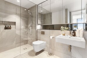 A modern bathroom with a glass-enclosed shower, a white toilet, and a sink with a mirror above it.