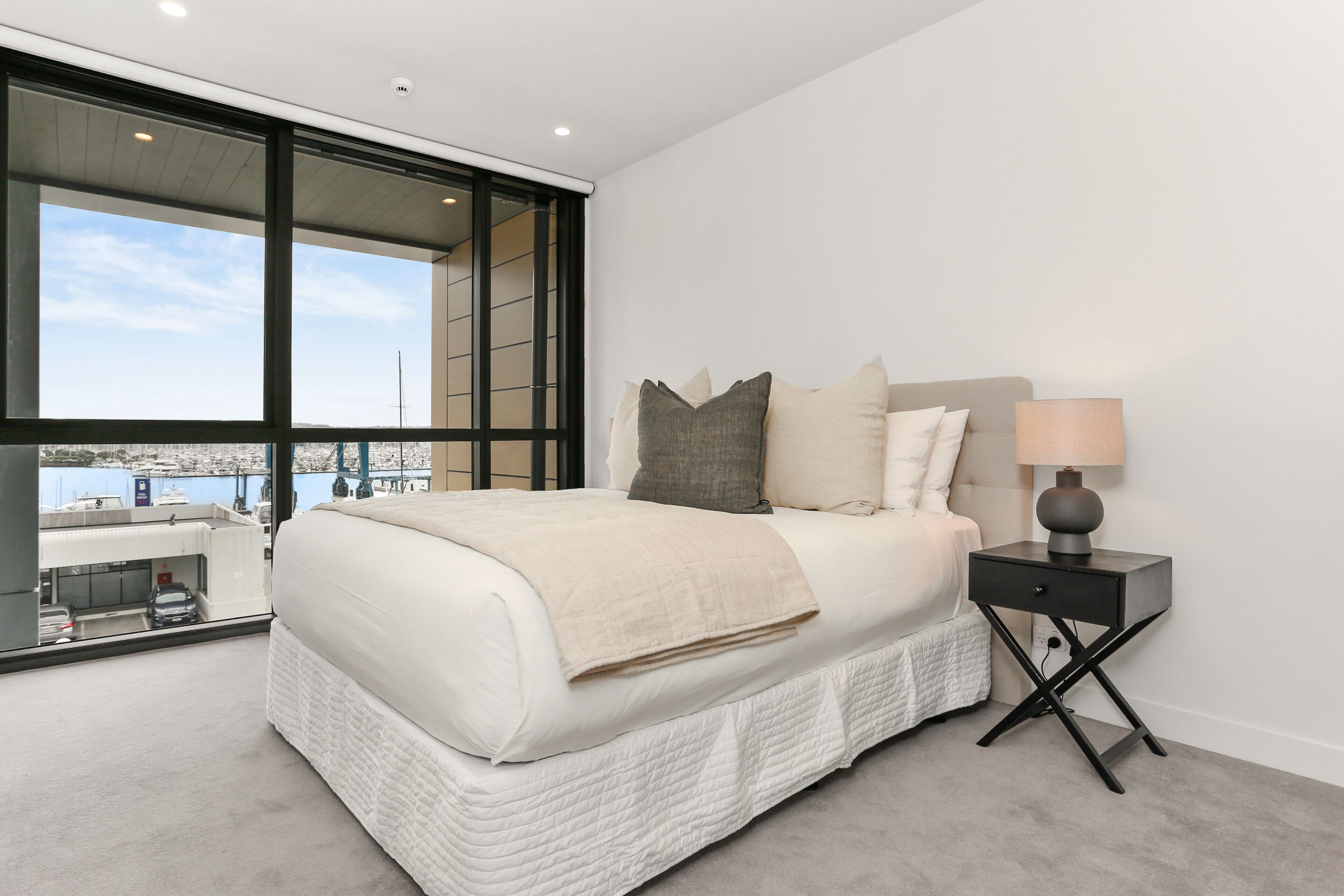 A modern bedroom with a large bed, a nightstand, and a view of the city.