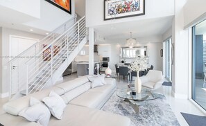 A modern living room with a white sofa, a glass coffee table, and a staircase with white railings.