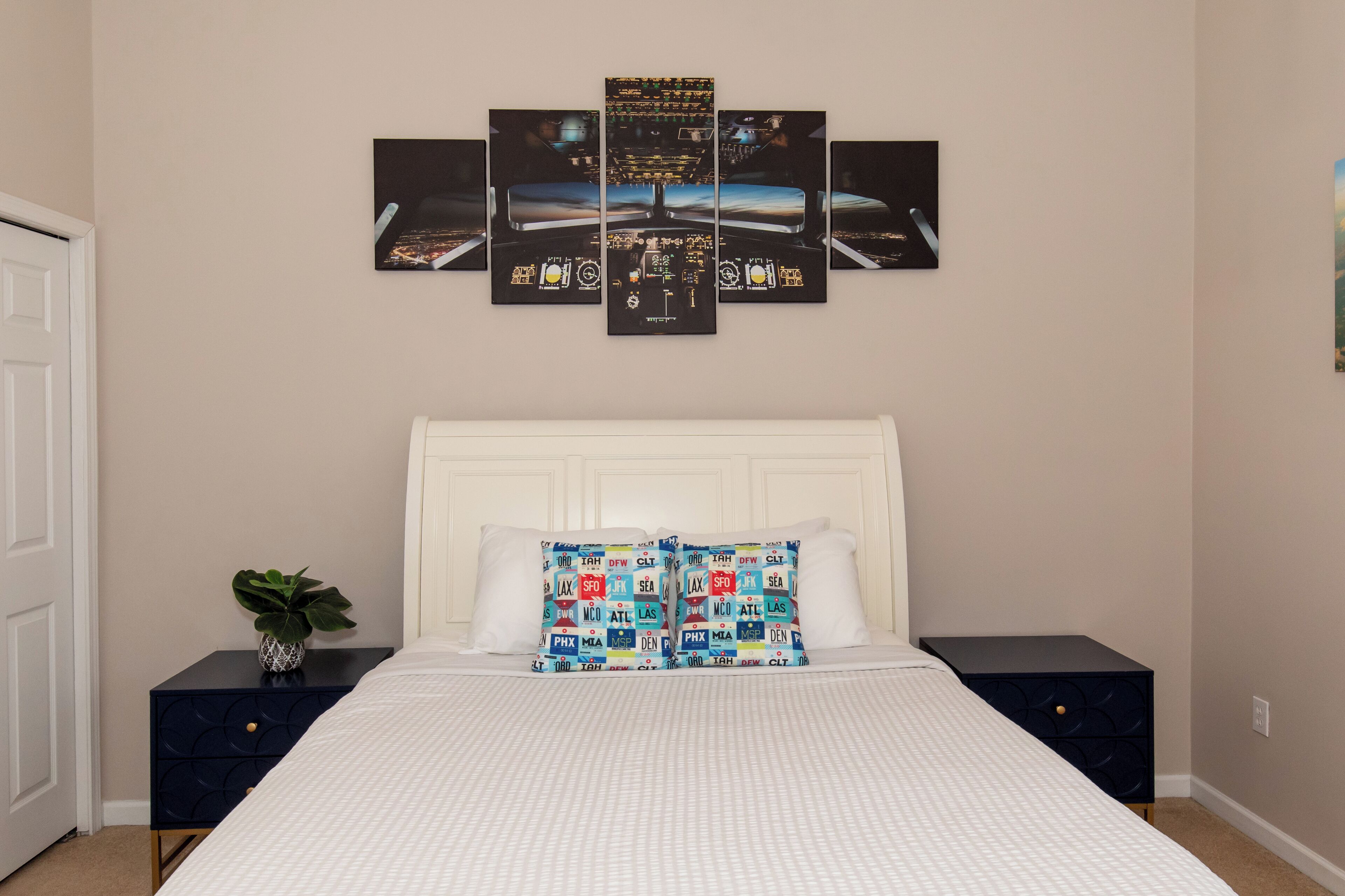Een keurig opgemaakte slaapkamer met een groot bed, een witte hoofdbord en twee nachtkastjes. Boven het bed hangt een stadsgezicht kunstwerk.