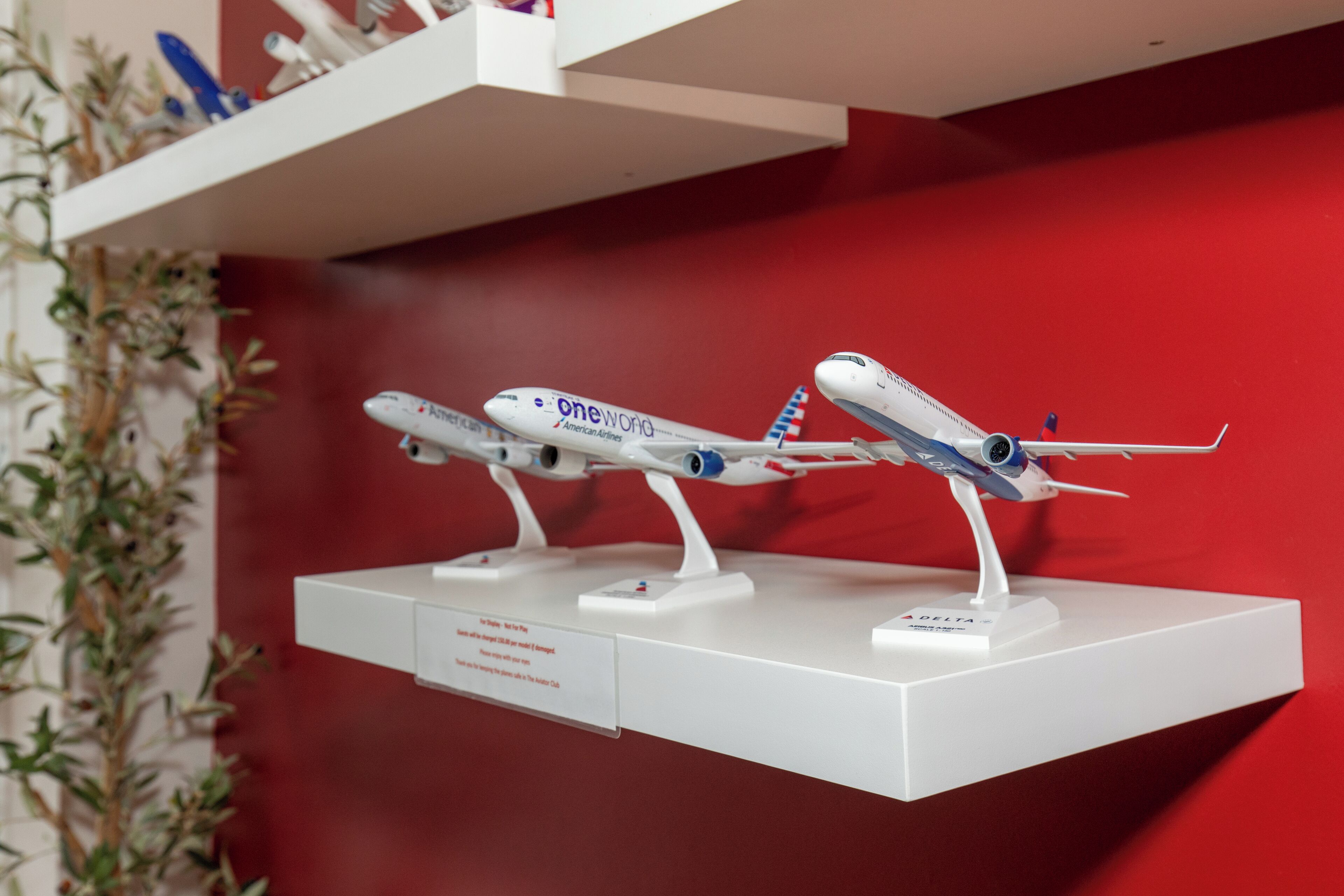 Una exhibición de modelos de aviones sobre un estante blanco frente a una pared roja.