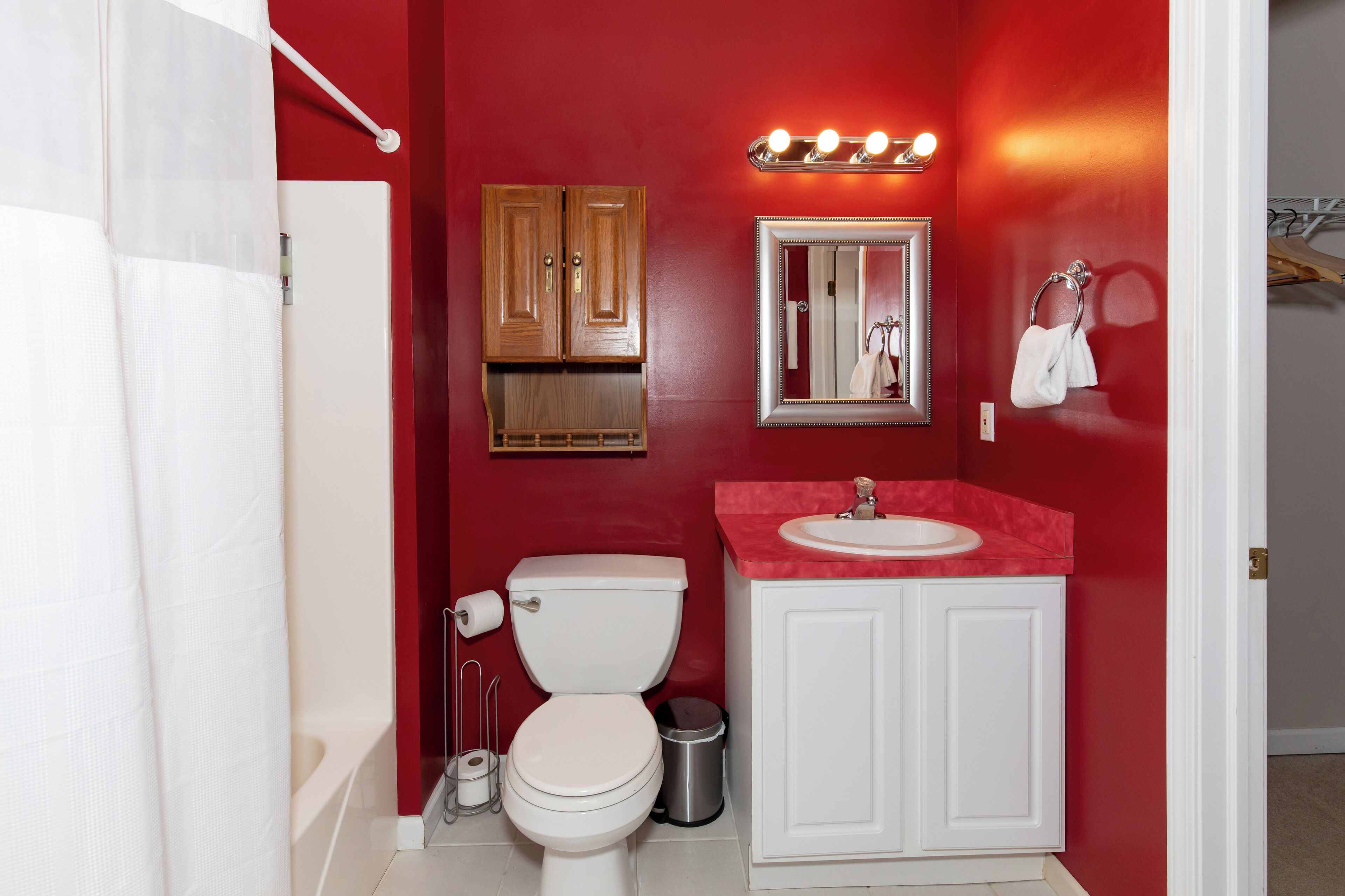 Un baño con pared roja, inodoro blanco y tocador con lavamanos.