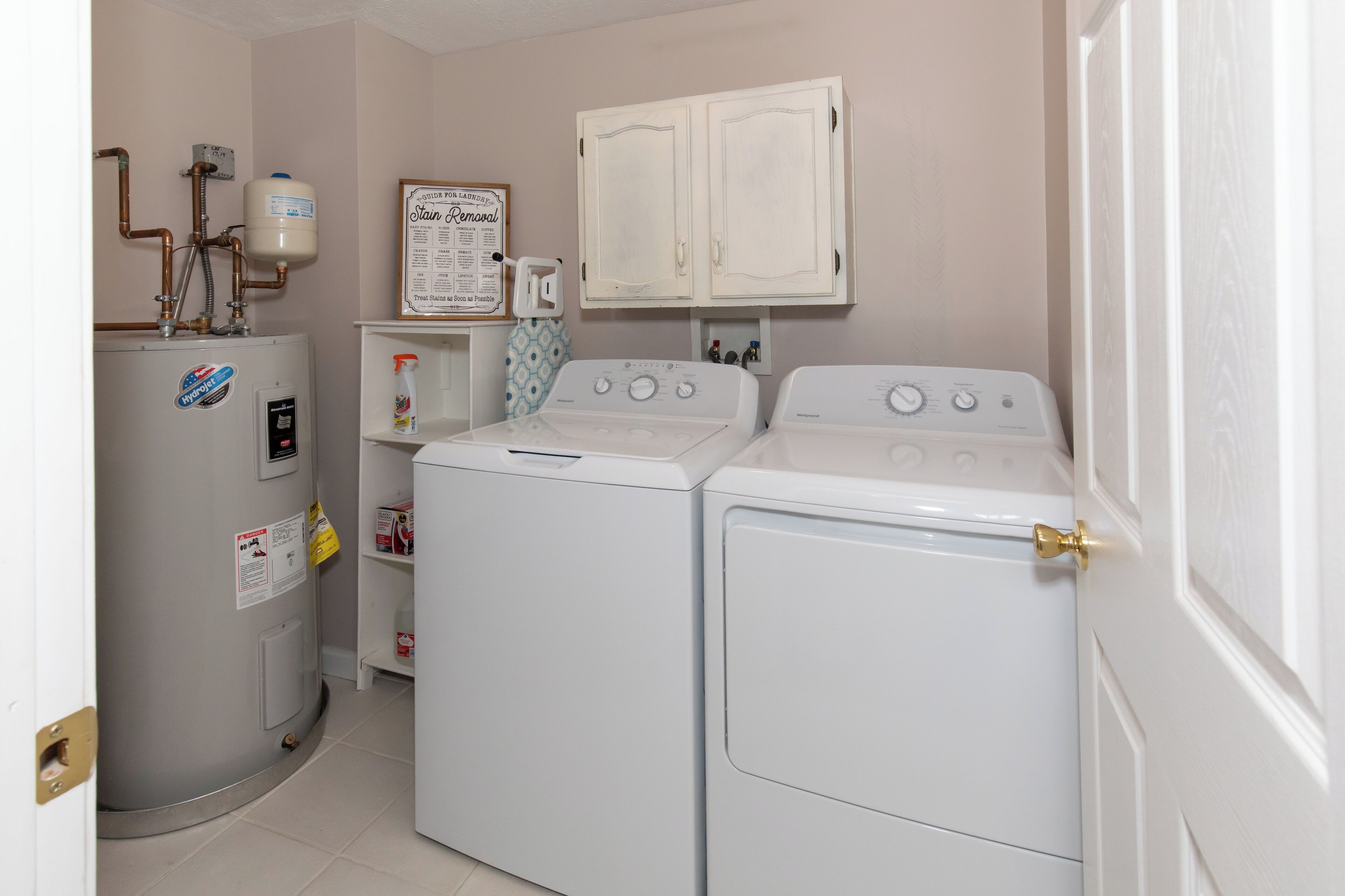 A laundry room with a water heater, two washing machines, a cabinet, and a wall-mounted sign.