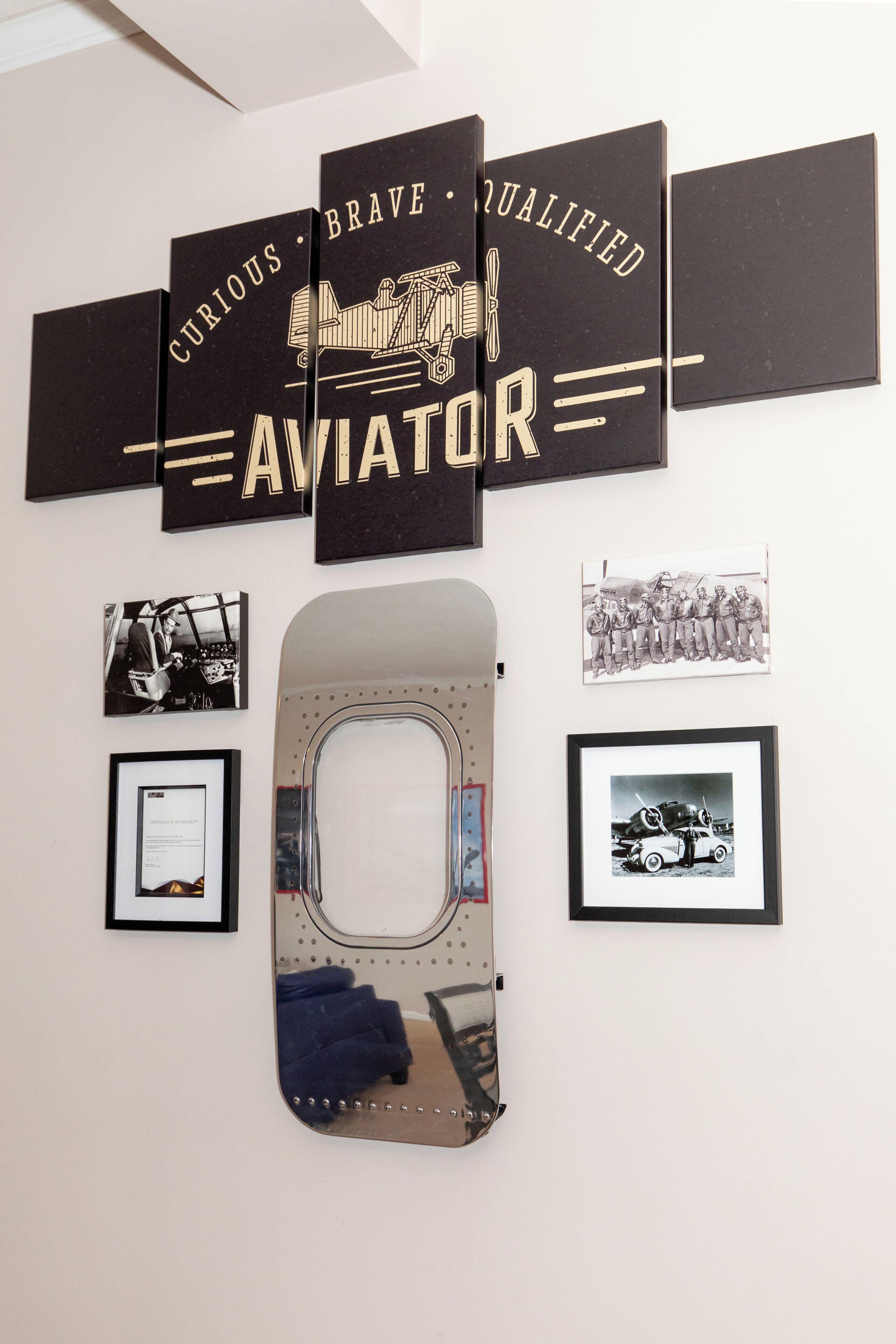 A wall with a large framed text reading "CURIOUS BRAVE QUALIFIED AVIATOR" and several framed photographs.