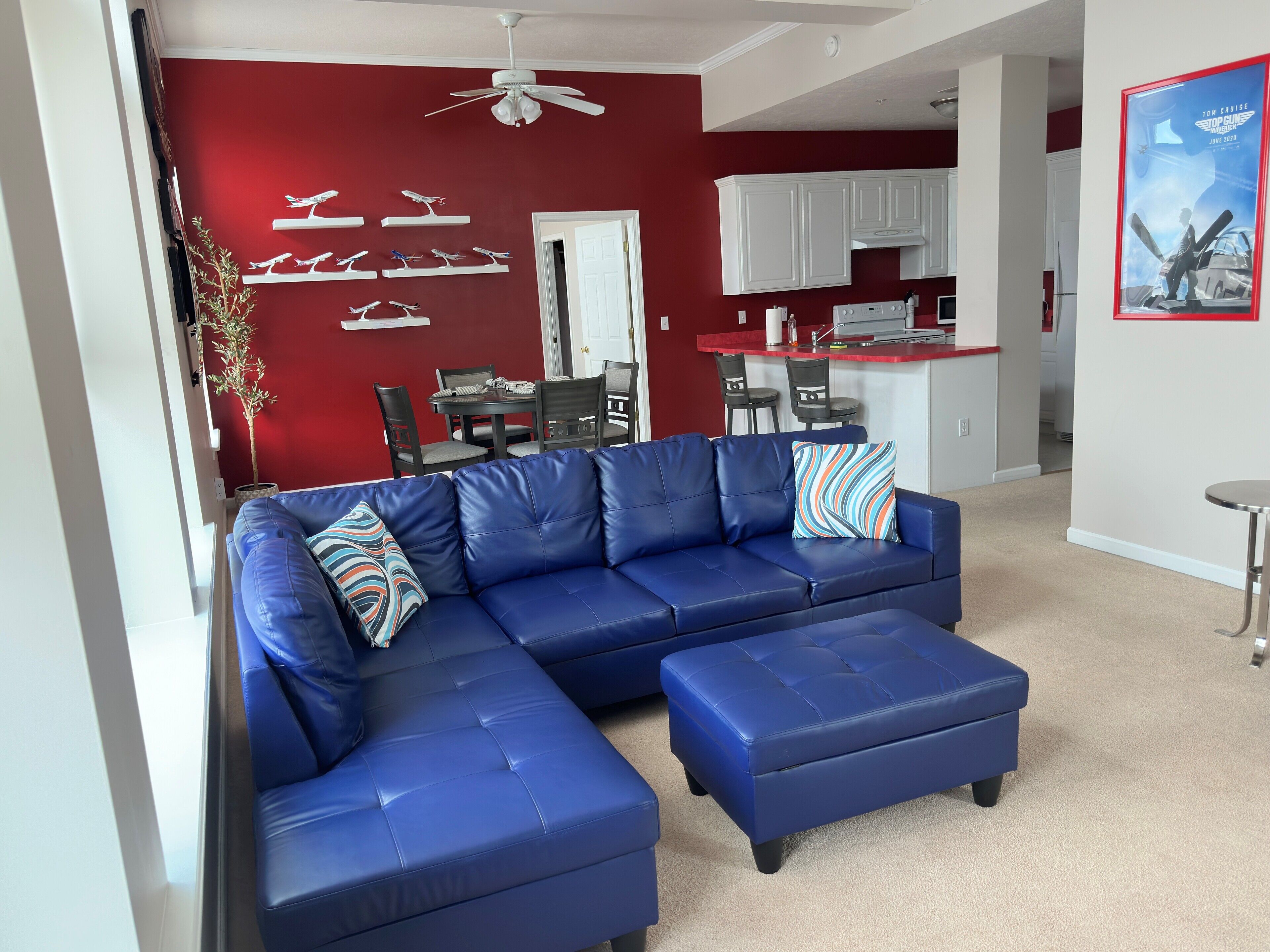 Una sala de estar con un sofá seccional azul, una zona de comedor con pared roja y una cocina con armarios blancos.