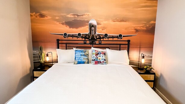 Une chambre à coucher avec un lit placé au centre, sous une fresque représentant un avion.