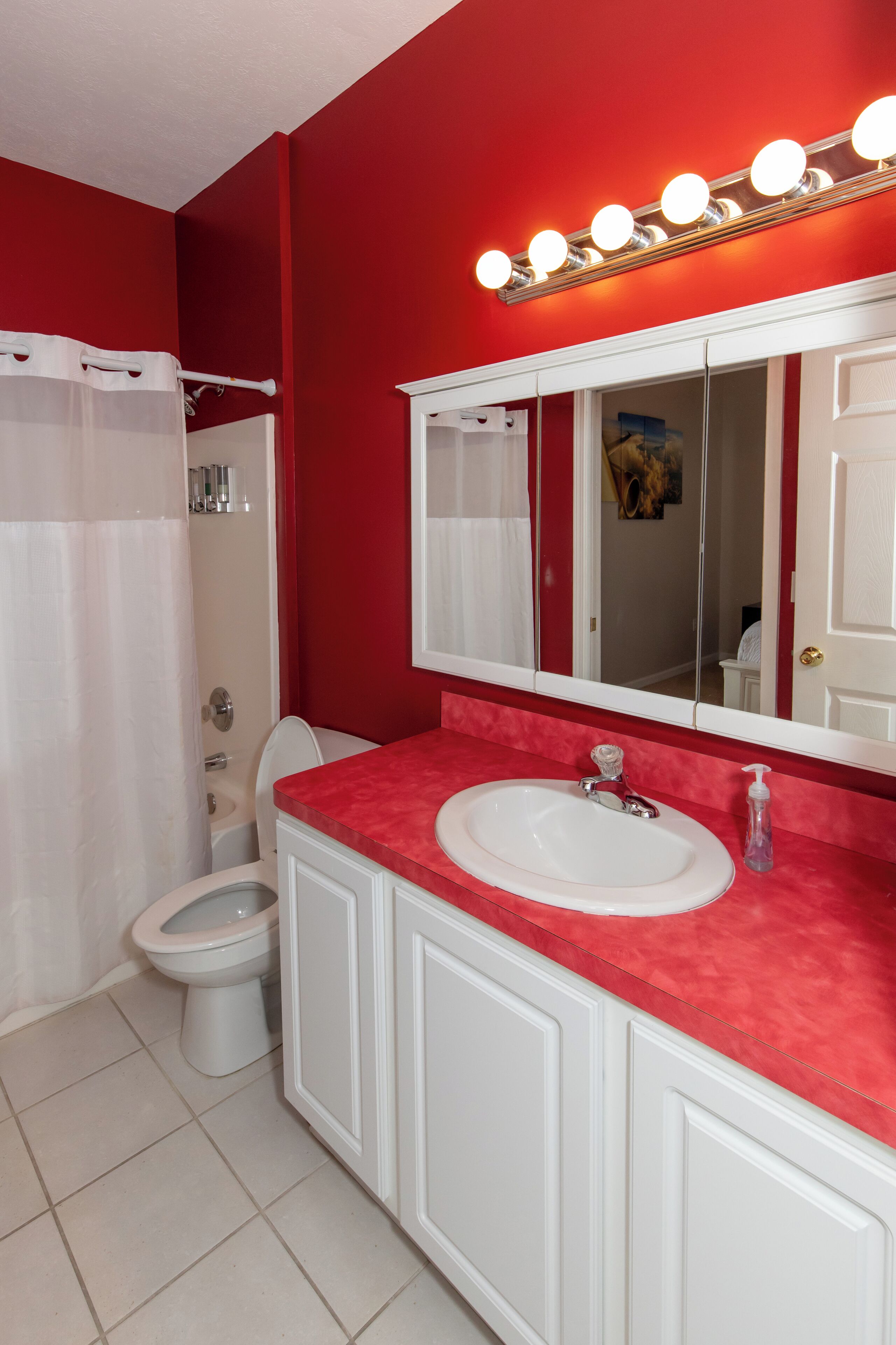 Une salle de bain avec un mur rouge, des accessoires blancs, un grand miroir et un rideau de douche.