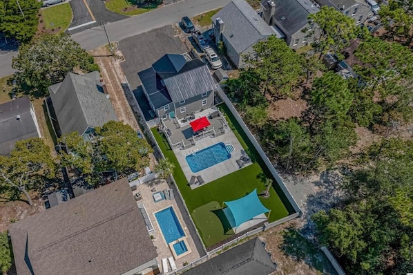 An aerial view of a residential property with a swimming pool, a tennis court, and a covered patio area.