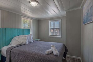 Een slaapkamer met een bed, twee ramen met zonwering, een schilderij aan de muur en een plafondlamp.