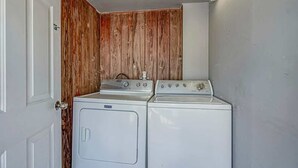 A laundry room with two washers and a dryer, wooden paneling on one wall, and a white door.