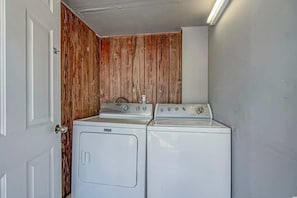 Une buanderie équipée de deux machines à laver et d’un sèche-linge, avec un lambris en bois sur un des murs et une porte blanche.