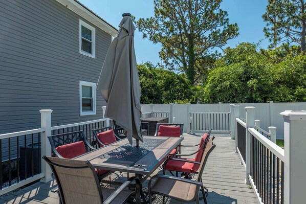 A deck with a table and chairs, a covered umbrella, and a white fence. - The Seven Oh Five | Coastal Duplex (North Myrtle Beach)
