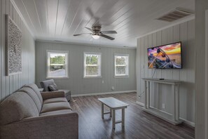 A living room with a ceiling fan, a sofa, a coffee table, and a TV mounted on the wall. - The Seven Oh Five | Coastal Duplex (North Myrtle Beach)