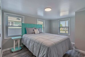 A bedroom with a bed, a small table, two windows, and a ceiling light.