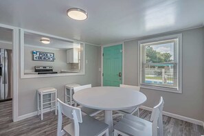A dining area with a round table and white chairs, a teal door, and a sign indicating a pool and beach. - Duplex 705 18th Ave S (North Myrtle Beach)