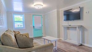 Sala de estar com sofá, uma mesa pequena, TV fixada num móvel branco e porta com moldura azul-turquesa.